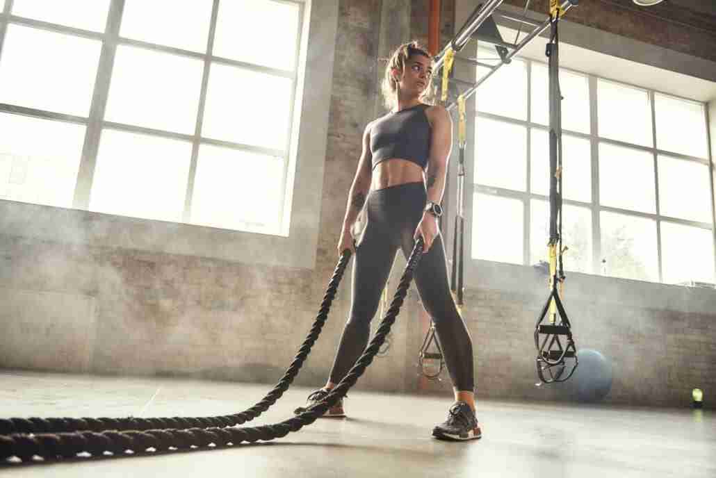 CrossFit training. Young athletic woman with perfect body doing crossfit exercises with a rope in with cross fit krav maga